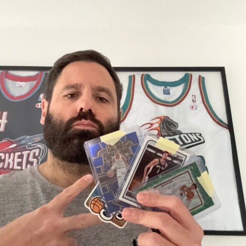 Kunde Len hält mehrere Basketball-Sammelkarten vor gerahmten NBA-Trikots